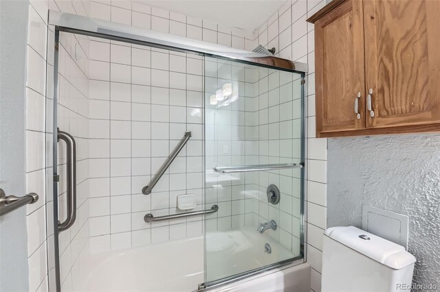 bathroom featuring combined bath / shower with glass door, toilet, and a textured wall