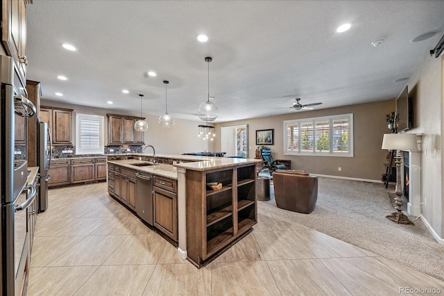 kitchen featuring appliances with stainless steel finishes, ceiling fan, sink, decorative light fixtures, and an island with sink