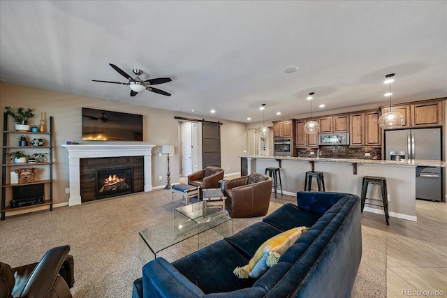 living room featuring ceiling fan, a barn door, a textured ceiling, and a tile fireplace