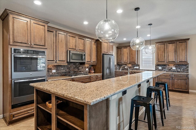 kitchen with light stone countertops, a kitchen bar, stainless steel appliances, a spacious island, and pendant lighting