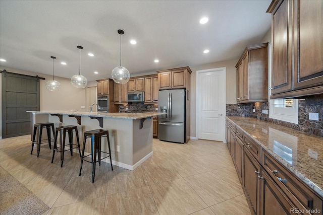 kitchen featuring a spacious island, a barn door, light stone countertops, appliances with stainless steel finishes, and decorative light fixtures