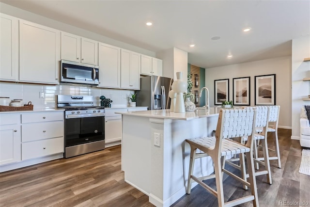 kitchen with a breakfast bar area, white cabinetry, a center island with sink, stainless steel appliances, and decorative backsplash