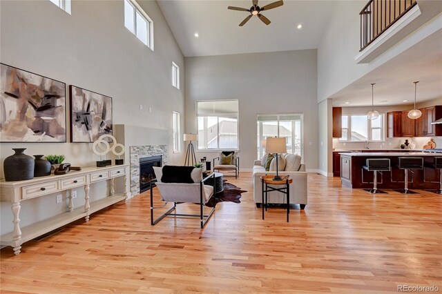 living room featuring a towering ceiling, a stone fireplace, and light hardwood / wood-style floors