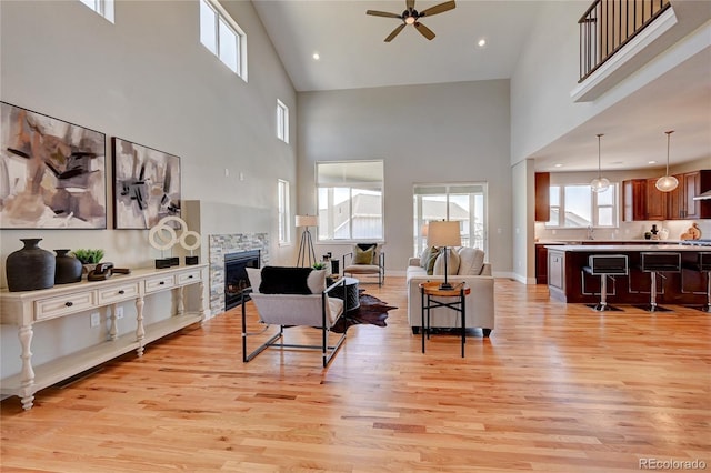 living room featuring a towering ceiling, a stone fireplace, and light hardwood / wood-style floors