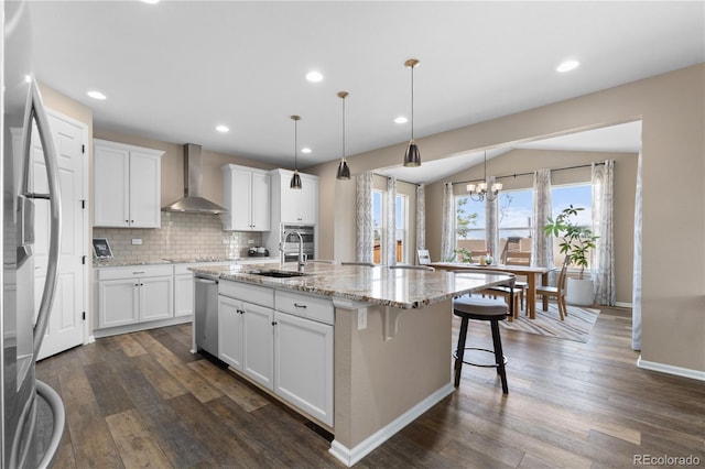 kitchen with wall chimney exhaust hood, a sink, a chandelier, appliances with stainless steel finishes, and white cabinets
