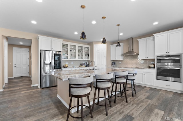 kitchen featuring stainless steel appliances, wall chimney range hood, a sink, decorative backsplash, and a kitchen island with sink