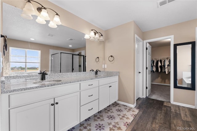 bathroom featuring wood finished floors, a stall shower, double vanity, baseboards, and a walk in closet