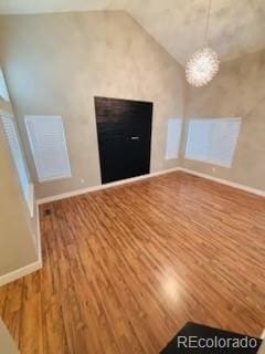 6973 Summerset Ave, Longmont, CO 80504 - unfurnished living room with vaulted ceiling, wood finished floors, baseboards, and a chandelier