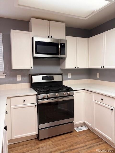 6973 Summerset Ave, Longmont, CO 80504 - kitchen with appliances with stainless steel finishes, white cabinetry, light wood finished floors, and light countertops