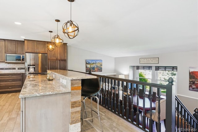 6537 S Brentwood Way, Littleton, CO 80123 - kitchen featuring appliances with stainless steel finishes, a kitchen island, light wood-style flooring, a kitchen bar, and light stone counters