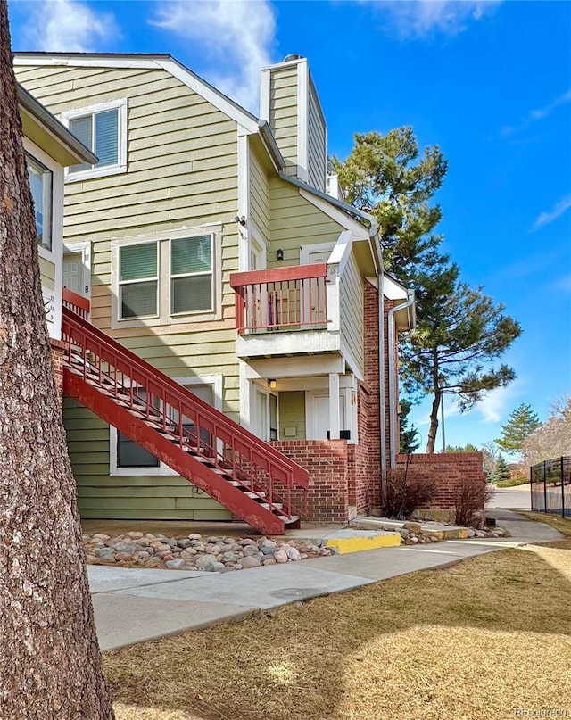 view of side of home featuring brick siding, stairway, a chimney, and a balcony