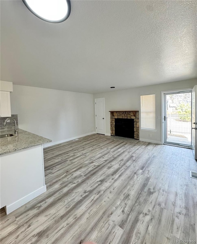 unfurnished living room with a sink, light wood-style flooring, a fireplace, and a textured ceiling