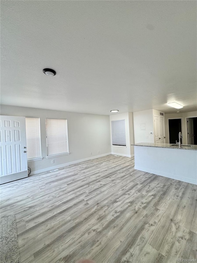 unfurnished living room with a sink, light wood-style flooring, baseboards, and a textured ceiling