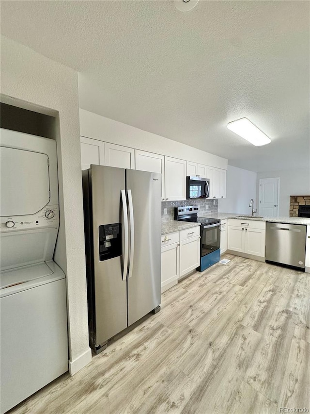 kitchen with a sink, light countertops, appliances with stainless steel finishes, light wood-type flooring, and stacked washing maching and dryer