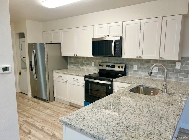 kitchen with stainless steel appliances, a sink, white cabinetry, and stacked washer / drying machine