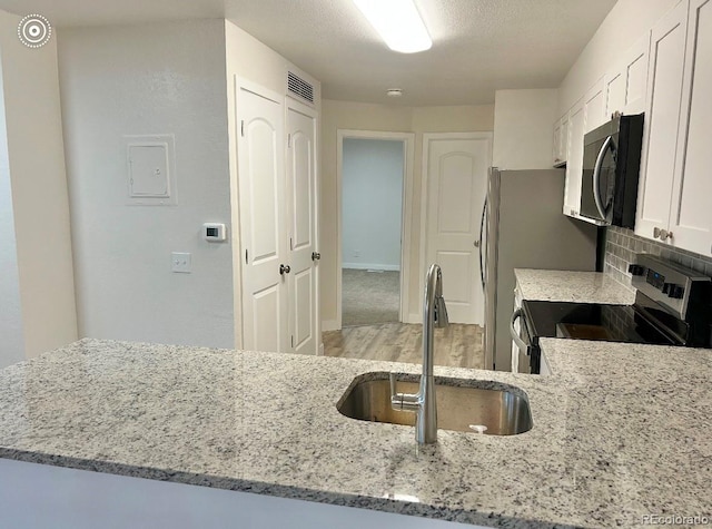 kitchen with a textured ceiling, light stone counters, a sink, white cabinets, and appliances with stainless steel finishes