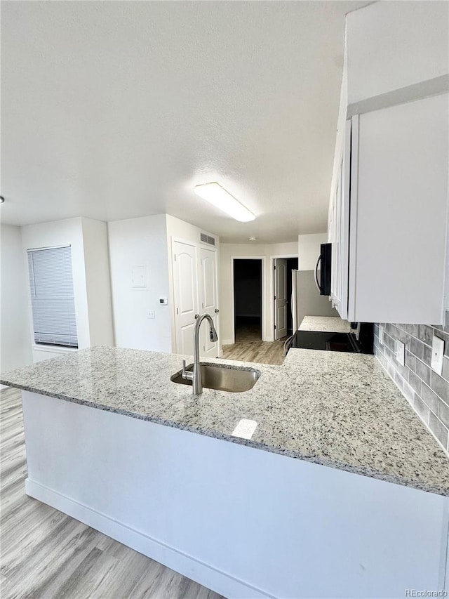 kitchen featuring light stone counters, light wood-style flooring, a sink, white cabinetry, and decorative backsplash