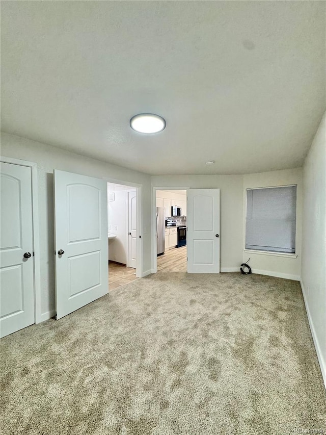 unfurnished bedroom with light carpet, baseboards, ensuite bathroom, and freestanding refrigerator