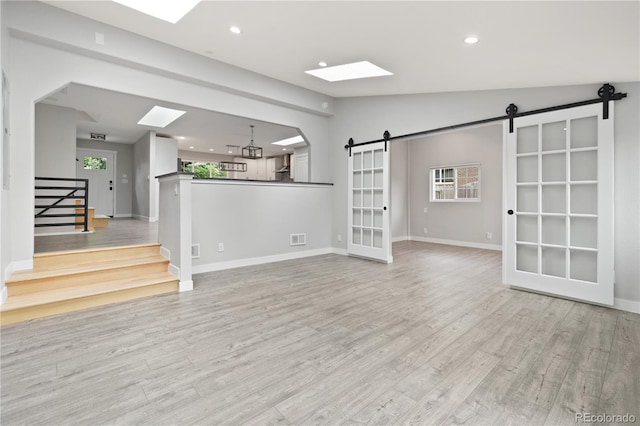 6451 S Hoyt St, Littleton, CO 80123 - unfurnished living room with a barn door, a skylight, light wood-style flooring, vaulted ceiling, and recessed lighting