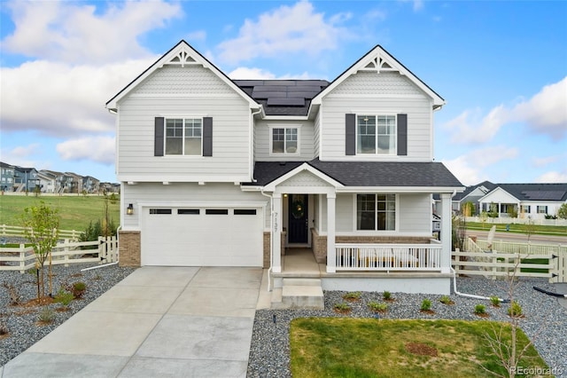 craftsman house with a porch, fence, roof mounted solar panels, concrete driveway, and an attached garage
