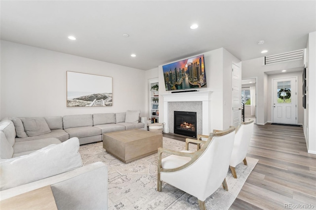living room featuring recessed lighting, light wood-style flooring, and a glass covered fireplace