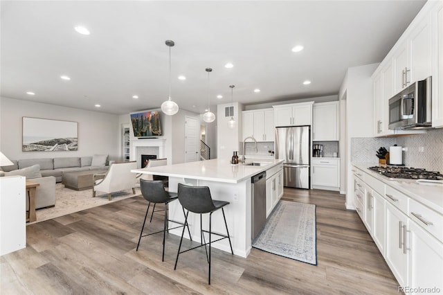 kitchen with appliances with stainless steel finishes, tasteful backsplash, a sink, open floor plan, and white cabinetry