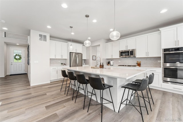 kitchen with a sink, light wood-style flooring, stainless steel appliances, backsplash, and visible vents
