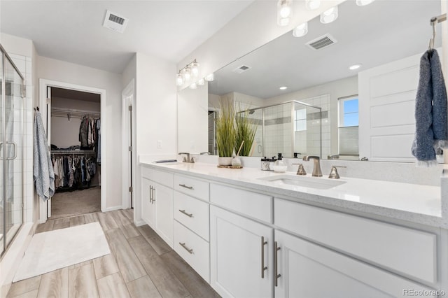 full bath with visible vents, a sink, a stall shower, and double vanity