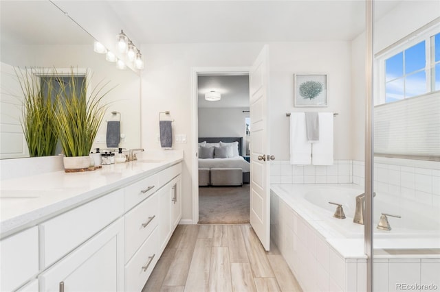 bathroom with double vanity, wood finished floors, connected bathroom, a bath, and a sink