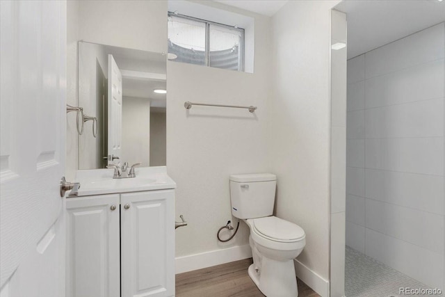 full bathroom featuring toilet, wood finished floors, a tile shower, baseboards, and vanity