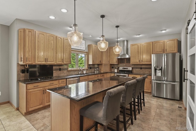 kitchen featuring stainless steel appliances, wall chimney exhaust hood, decorative light fixtures, a kitchen island, and a barn door