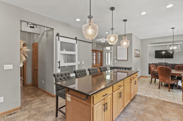 kitchen featuring dark stone counters, a center island, a barn door, a kitchen breakfast bar, and decorative light fixtures