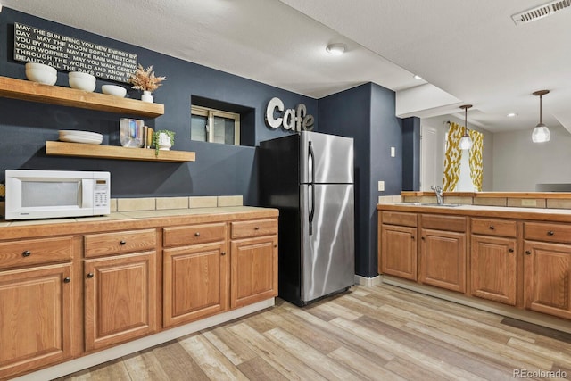 kitchen with light hardwood / wood-style floors, tile countertops, sink, stainless steel fridge, and pendant lighting