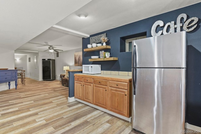 kitchen with tile countertops, a textured ceiling, ceiling fan, light wood-type flooring, and stainless steel fridge