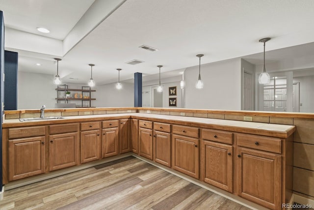 kitchen featuring tile countertops, pendant lighting, sink, and light hardwood / wood-style floors