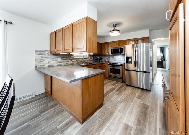 kitchen featuring visible vents, a sink, a peninsula, brown cabinetry, and stainless steel appliances
