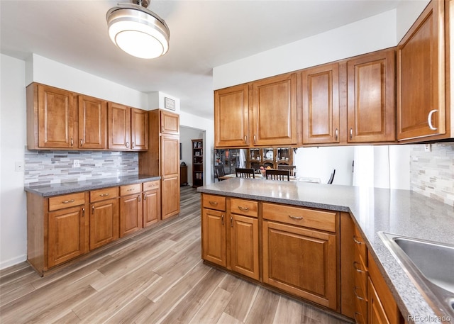kitchen with tasteful backsplash, a peninsula, a sink, and brown cabinetry