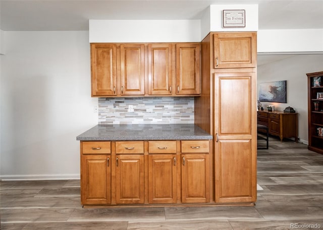 kitchen with brown cabinets, decorative backsplash, dark stone counters, and baseboards