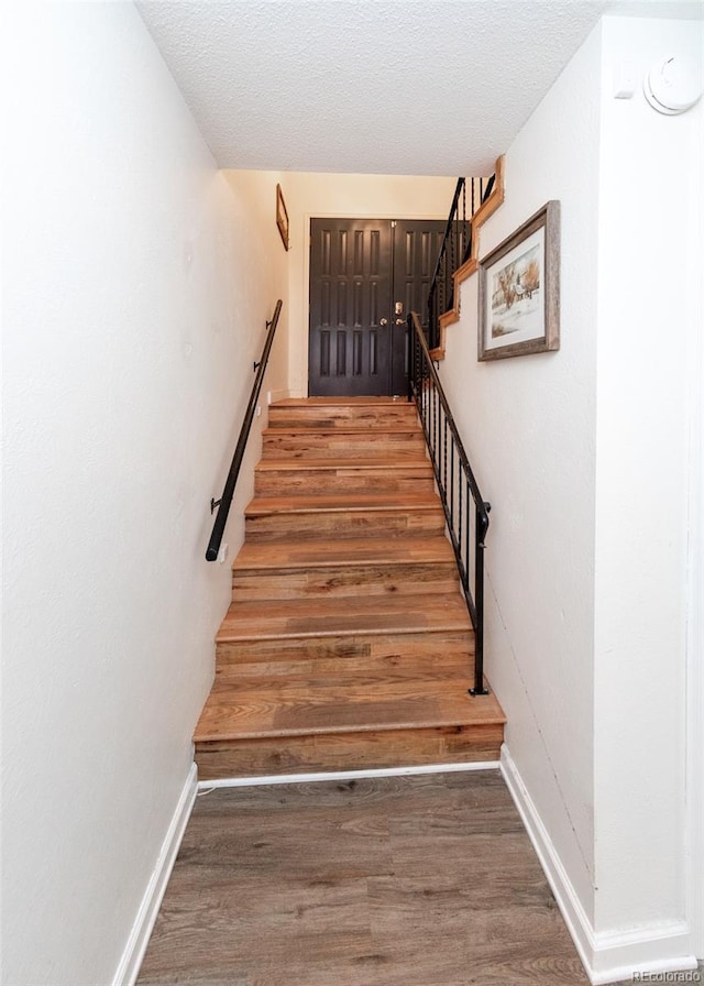 staircase with a textured ceiling, wood finished floors, and baseboards