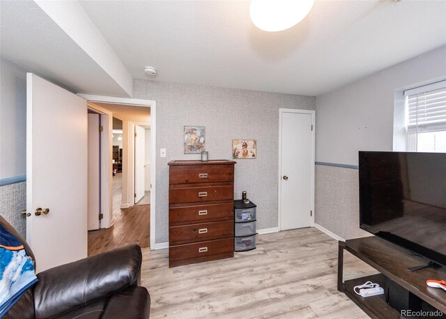 living area featuring light wood-style floors, wallpapered walls, baseboards, and a wainscoted wall