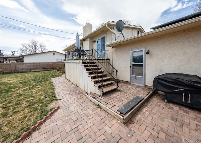 back of house featuring a patio area, a lawn, a chimney, fence, and stucco siding