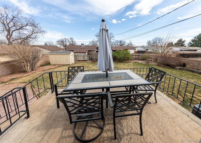 wooden deck featuring an outbuilding, outdoor dining area, a lawn, and a storage unit