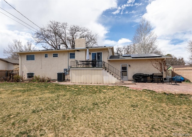 rear view of property featuring stucco siding, a lawn, a patio area, fence, and solar panels