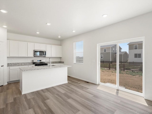 4694 Sugarcane St, Johnstown, CO 80534 - kitchen featuring appliances with stainless steel finishes, light wood finished floors, white cabinetry, a center island with sink, and recessed lighting