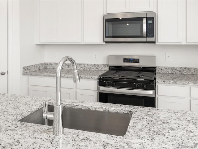 4694 Sugarcane St, Johnstown, CO 80534 - kitchen featuring appliances with stainless steel finishes, white cabinetry, and light stone counters