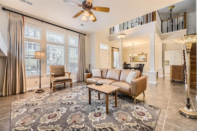 living room with ceiling fan with notable chandelier, baseboards, visible vents, and ornate columns