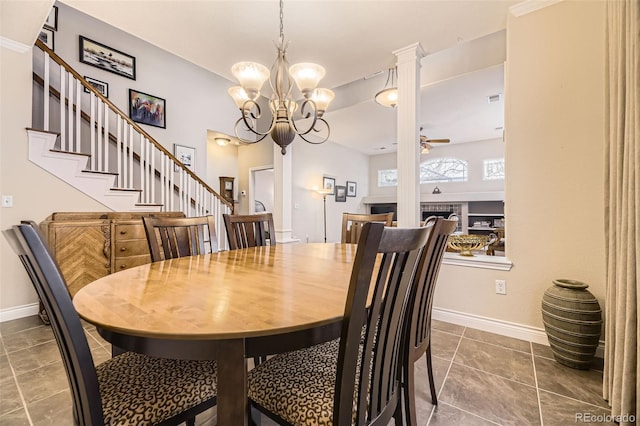 dining area featuring ceiling fan with notable chandelier, dark tile patterned flooring, a fireplace, baseboards, and stairway