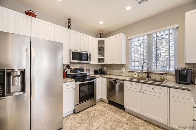 kitchen featuring glass insert cabinets, stainless steel appliances, light countertops, white cabinetry, and a sink