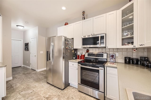 kitchen with light countertops, backsplash, appliances with stainless steel finishes, glass insert cabinets, and white cabinets