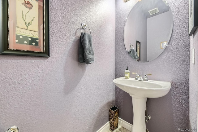 bathroom featuring visible vents, a textured wall, a sink, and baseboards